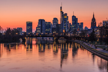 Fototapeta na wymiar Frankfurt skyline in the evening. Sunset turns the sky orange-red. Reflections from illuminated houses from the financial district in the river Main