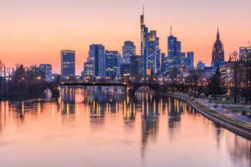 Fototapeta na wymiar Frankfurt skyline in the evening. Commercial buildings from the financial district with lights and reflections in the water of the river Main at sunset. Bridge in the foreground.