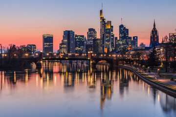 Fototapeta na wymiar Frankfurt skyline in the evening at sunset. High-rise buildings from the financial district and river Main with reflections. Illuminated houses and bridge