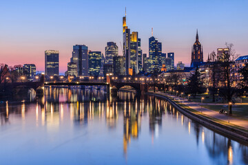 Fototapeta na wymiar Frankfurt city skyline in the evening after sunset. Illuminated buildings of high-rise buildings from the business and financial center. Bridge over the river Main with street lights