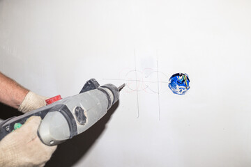 A worker with a drill drills a wall. Additional electrical outlet in the room. Repair and...