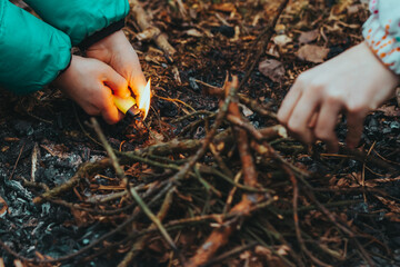 Children's hands light fire to fire in forest with lighter. Naughty child playing with cigarette lighter