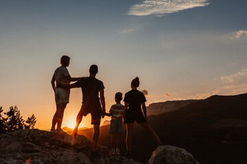 Friendly embracing family with two kids, a son and daughter, stand on top of mountain and watch...
