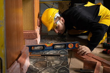 A construction worker checks with a spirit level that the terracotta tiles are evenly placed in all...