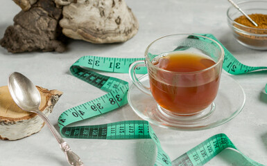 Chaga birch mushroom is a trendy superfood for diet and immunity. Natural tea, coffee and pieces of birch chaga in a glass cup, measuring tape on a light background. Naturopathy. Natural antioxidant.