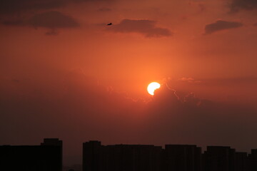 Obraz premium Sunset over the city. Sunset city scenery with sun. City silhouette against the sky on a sunset. Sun hiding behind the cloud.