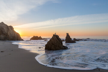Fototapeta na wymiar white foamy waves on rocky Malibu Beach in California at sunrise