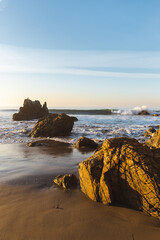 Vertical shot of rocks on sandy beach with approaching waves in Malibu, California