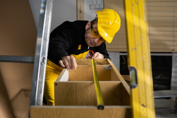 A construction worker checks a pull-out cupboard at the top with a tape measure. Wearing personal...