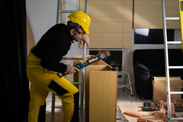 The builder checks with a spirit level that the cabinet is made correctly and without deviations. Construction worker wearing personal protective equipment.