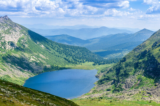 Taiga. Siberia. A daytime landscape with a lake among the mountains and clouds in the blue sky. Ergaki. Western Sayan.
