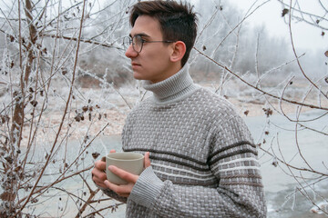 A young guy is drinking tea on the street. Winter landscape.