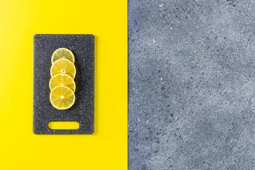 Kreativer Lebensmittelhintergrund in ultimativem Grau und leuchtender Trendfarbe. Zitrone und Schneidebrett auf grauer und gelber Tischoberfläche © Victoria Kondysenko