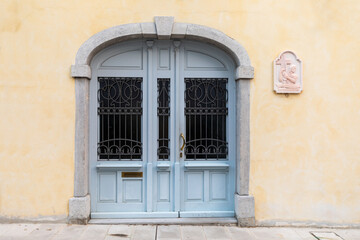 Porta chiusa molto vecchia su facciata di muro giallo con bassorilievo di gesu che porta il crocifisso.