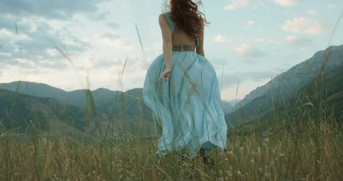 Woman in white dress running on a mountain with raised hands while wind is blowing her dress and red hair - freedom, nature concept 4k footage