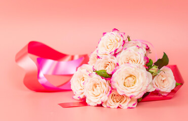 delicate bouquet of bushy peony roses with bright ribbons in the shape of hearts on a pink background, the concept of congratulations on Valentine's day