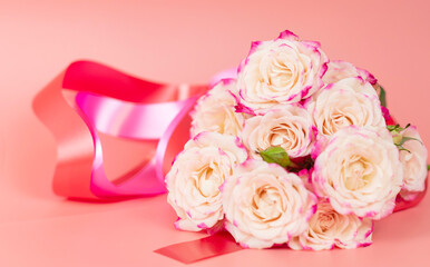 delicate bouquet of bushy peony roses with bright ribbons in the shape of hearts on a pink background, the concept of congratulations on Valentine's day