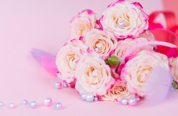 delicate bouquet of bushy peony roses with bright ribbons, pearls, feathers and hearts  on a pink background, the concept of congratulations on Valentine's day