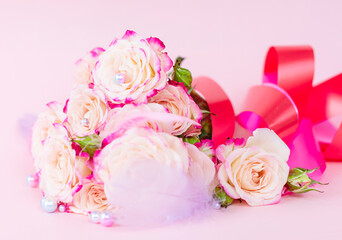 Fototapeta premium delicate bouquet of bushy peony roses with bright ribbons, pearls, feathers and hearts on a pink background, the concept of congratulations on Valentine's day