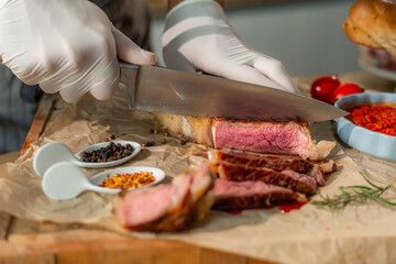 A close-up view of a cook cutting a grilled steak into thinner pieces on a wooden kitchen board