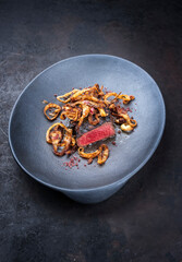 Modern style traditional dry aged sliced beef tenderloin with fried onion rings and red wine salt served as top view on a design plate with copy space