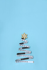 Measuring tape in the form of Christmas tree and New Year's toy on light blue background. Minimal concept of balanced diet for holidays. Vertical poster. Copy space