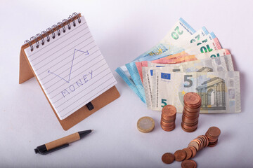 Vista desde arriba de una libreta de notas, monedas de céntimos de euro amontonadas y billetes.