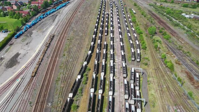 Aerial footage of a lot of hopper car / hopper wagon old rusty train cargo trucks on train tracks located in the town of York in West Yorkshire in the UK on a bright summers day
