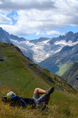 Fototapeta premium Hiker resting on grass near ski station Les deux Alpes and view on Alpine mountains peaks in summer, Isere, France
