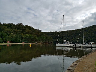 Beautiful early morning view of a creek with reflections of boats, mountains, trees and dark clouds, Cowan Creek, Bobbin Head, Ku-ring-gai Chase National Park, New South Wales, Australia
