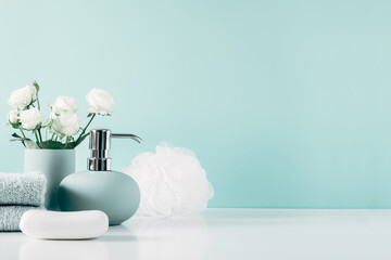Soft light bathroom decor in mint color, towel, soap dispenser, white roses flowers, accessories on pastel mint background. Elegant decor bathroom interior.