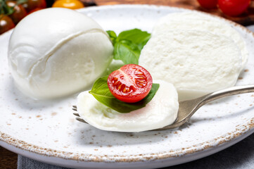 Cheese collection, eating. of white soft Italian cheese mozzarella, served with red cherry tomatoes, fresh basil leaves