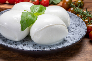 Cheese collection, white balls of soft Italian cheese mozzarella, served with red cherry tomatoes, fresh basil leaves