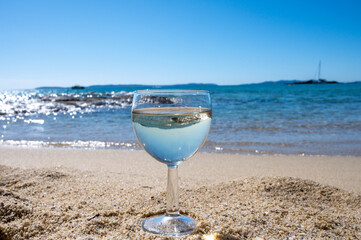Glass of local dry white wine on white sandy beach and blue Mediterranean sea on background, near Le Lavandou, Provence, France
