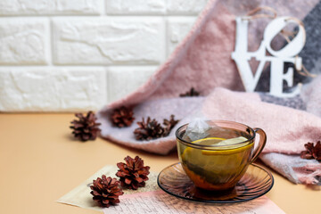 Green tea with lemon in a transparent dark mug on a yellow background and a knitted scarf with a wooden sign LOVE. Cozy wallpapers, Home atmosphere, Copy Space