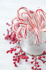 Original Christmas still life photograph of red and white candy canes in a white pot on a bright white background with red berries