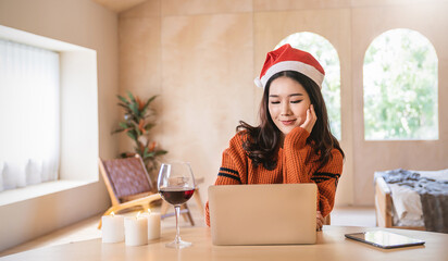 Portrait of business asian woman online working in bedroom desk use computer. Freelance online marketing, young happy girl video call on laptop toasting with wine celebrating Christmas alone at home.