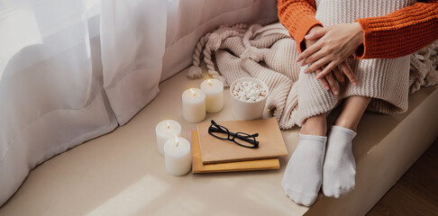 Cup of coffee and candle cozy bed with book and blanket. Warm woolen sweater in cold autumn or winter weekend, warm cocoa with marshmellows. Lazy day, Cosy scene, hygge concept banner
