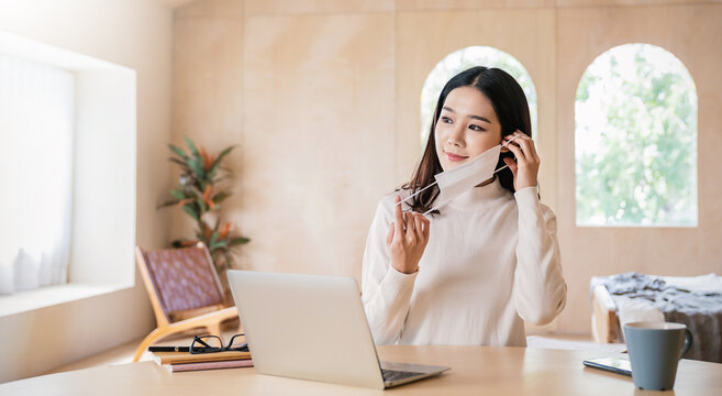 Portrait Of Sme Business Asian Woman Wears Medical Protective Mask Working From Home At The Computer Desktop. Self Isolation Quarantine In Winter. Coronavirus Lockdown And Flu Covid Epidemic.