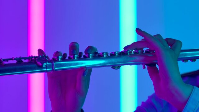 Musical concert of classical music performed by a professional female flutist. Female hands with a flute close up. Wind instrument against the background of bright neon lights. Slow motion.