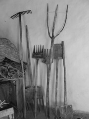 Black and white photograph of wooden farming and agriculture tools including harrow and shovel in a country house in front of a white wall.