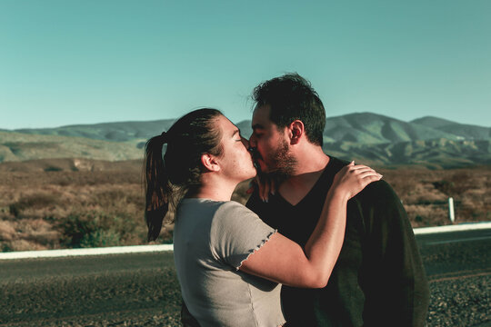 Side view portrait of a amazing couple kissing against sunset outside while traveling in their vacation time. Mexican couple kissing mountains view behind them