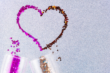 Heart shape made of multicolored glitter. Two champagne glasses with splash of heart shaped confetti over ultimate gray glitter background. Valentine's Day concept. Copy space. Top view