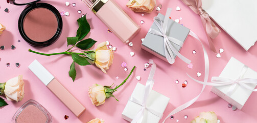 Creative composition with flowers, decorative cosmetic products, gift boxes and shining heart-shaped decorations on pink pastel background top view. St. Valentine’s Day concept. Woman’s Day background