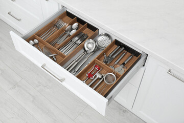 Open drawer with different utensils and cutlery in kitchen, above view