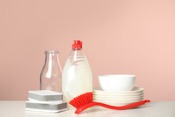 Cleaning supplies for dish washing and plates on white table against pink background
