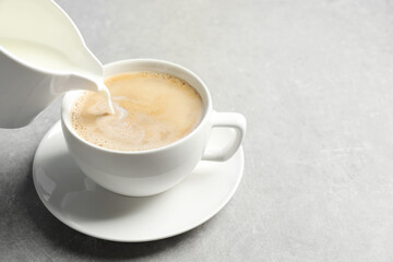 Pouring milk into cup of hot coffee on grey table, space for text