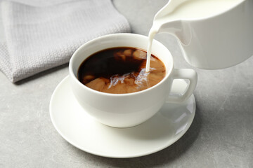 Pouring milk into cup of hot coffee on grey table