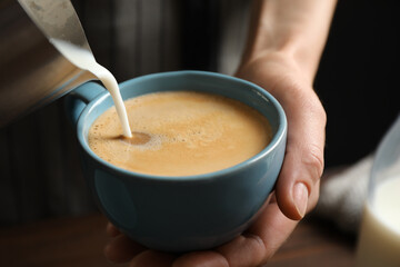 Woman pouring milk into cup of hot coffee, closeup