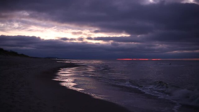 Cold winter windy Baltic sea coast beach in twilight purple light with dramatic cloudy sky and tranquil romantic waves. An HD video footage with audio